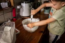 Menino chicoteando e misturando bolo de manteiga em tigela branca com w — Fotografia de Stock