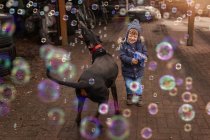 Toddler playing with doberman pincher and bubbles and bubble gun — Stock Photo