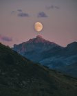 Luna saliendo durante la puesta del sol alineada con la cima de la montaña, Pirineos. - foto de stock