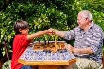 Дедушка и внук пожимают друг другу руки над шахматной доской — стоковое фото
