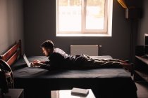 Homem usando computador portátil deitado na cama em casa — Fotografia de Stock