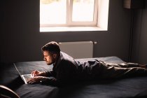 Чоловік за допомогою портативного комп'ютера лежить на ліжку вдома — стокове фото