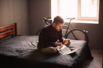 Человек с ноутбуком сидит на кровати дома — стоковое фото