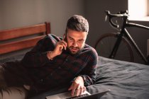 Чоловік розмовляє на смартфоні, використовуючи ноутбук, який працює вдома — стокове фото