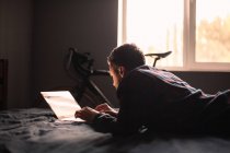 Чоловік за допомогою портативного комп'ютера лежить на ліжку вдома — стокове фото