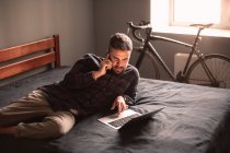 Чоловік розмовляє на смартфоні, використовуючи ноутбук, який працює вдома — стокове фото