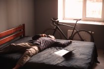 Уставший мужчина разговаривает по смартфону лежа на кровати дома — стоковое фото