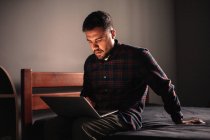 Mann sitzt mit Laptop zu Hause im Bett — Stockfoto