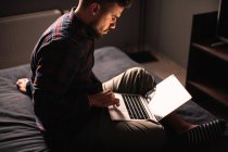 Mann sitzt mit Laptop zu Hause im Bett — Stockfoto