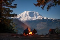 Coppia di campeggio seduto nel campo in una calda giornata invernale con tenda e un falò sullo sfondo — Foto stock