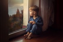 Маленький мальчик в голубой одежде сидит на полу у окна и туалета — стоковое фото