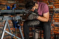 Junge erwachsene Mechaniker sitzen auf Stuhl und prüfen sorgfältig die Verkabelung, die am Steuer eines Elektrorollers in seiner Werkstatt läuft. — Stockfoto