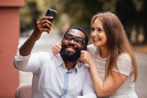 The beautiful young couple of diverse people are taking a photo at a smartphone in the city — Stock Photo