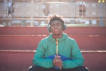 Hintergrundbeleuchtung Porträt eines jungen schwarzen Mannes, der sich entspannt, während er Musik in der Stadt hört. — Stockfoto