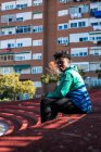 Ritratto di un giovane ragazzo nero seduto in città. Sfondo blocco di appartamenti. — Foto stock