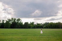 Young woman in a white dress with a backpack on the field — Stock Photo