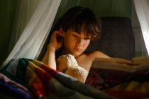 Bambina che legge libro a letto — Foto stock