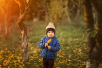 Retrato de un niño pequeño en el jardín con chaqueta azul sosteniendo un colmillo - foto de stock