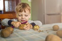 Маленький блондинка вчиться очищати картоплю з ситі — стокове фото