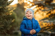 Niño pequeño con ojos azules y chaqueta azul riendo en el bosque - foto de stock