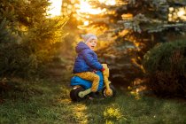 Niño pequeño con ojos azules y chaqueta azul sentado en juguete de plástico - foto de stock