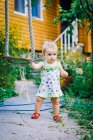 Cute baby girl 3-4 year old in the garden plays a rustic swing — Stock Photo
