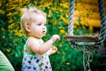 Linda niña de 3-4 años en el jardín juega un swing rústico - foto de stock