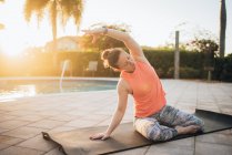 Uma mulher fazendo esteira pilates e alongamento ao lado de uma piscina ao nascer do sol — Fotografia de Stock
