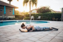 Жінка робить килимові палі біля басейну на сході сонця влітку — стокове фото