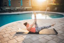 Une femme faisant tapis pilates à côté d'une piscine au lever du soleil en été — Photo de stock
