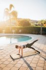 A woman doing mat pilates next to a pool at sunrise in the summer — Stock Photo