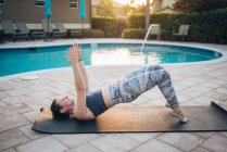 A woman doing mat pilates & glute bridges next to a pool at sunrise — Stock Photo