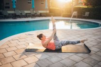 Una donna che fa pilates mat accanto a una piscina all'alba in estate — Foto stock