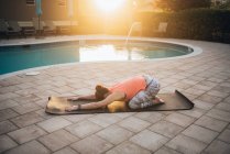 Женщина занимается пилатесом и растягивается рядом с бассейном на рассвете — стоковое фото