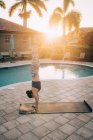 Женщина делает стойку на руках и мат пилатес рядом с бассейном на рассвете — стоковое фото