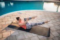 Una donna che fa pilates mat accanto a una piscina all'alba in estate — Foto stock