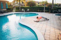 Uma mulher fazendo esteira pilates & pranchas ao lado de uma piscina ao nascer do sol — Fotografia de Stock
