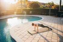 A woman doing mat pilates & planks next to a pool at sunrise — Stock Photo