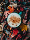 Overhead of pumpkin spice latte on plaid fall scarf with leaves — Stock Photo