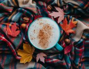 Overhead of pumpkin spice latte on plaid fall scarf with leaves. — Stock Photo