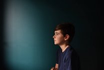 Portrait of a sad young boy against a dark blue wall. — Stock Photo