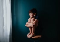 Niño feliz sentado en un taburete contra una pared azul oscuro. - foto de stock