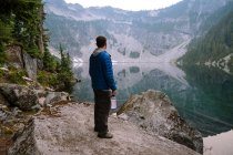 Homme en veste bouffie bleue debout à côté du lac vierge — Photo de stock