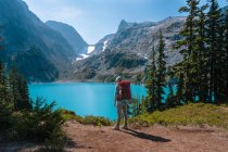 Female with backpack standing next to gorgeous alpine lake — Stock Photo