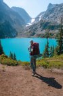 Female with backpack standing next to amazing blue colored alpine lake — Stock Photo