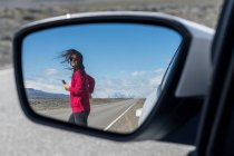 Mujer cruzando la ruta vista a través del espejo retrovisor del coche - foto de stock