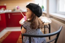 Giovane ragazza con un berretto nero seduto al tavolo della cucina. — Foto stock