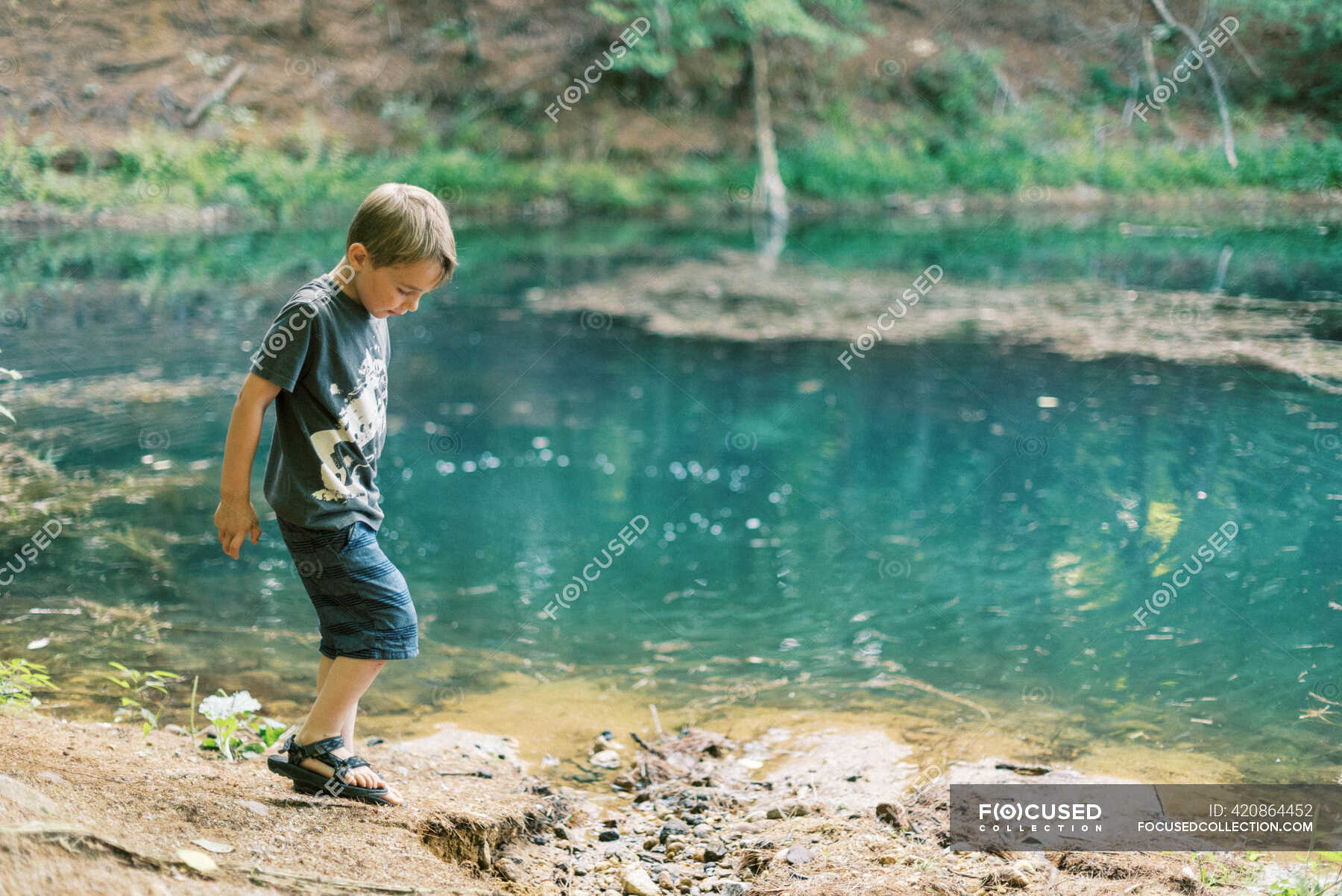 a-five-year-old-boy-playing-by-a-turquoise-pond-in-the-woods-curious