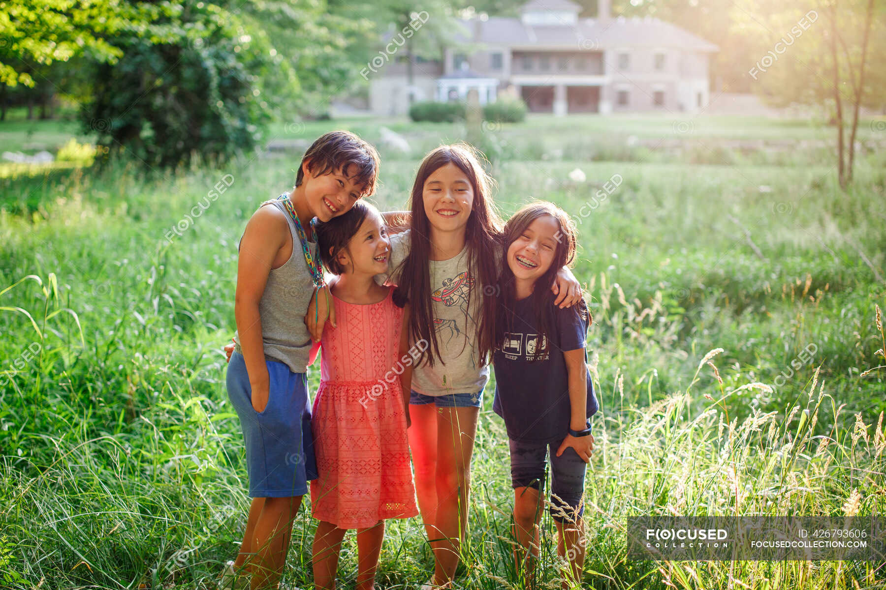 Happy children stand with arms around each other in sunlit field ...