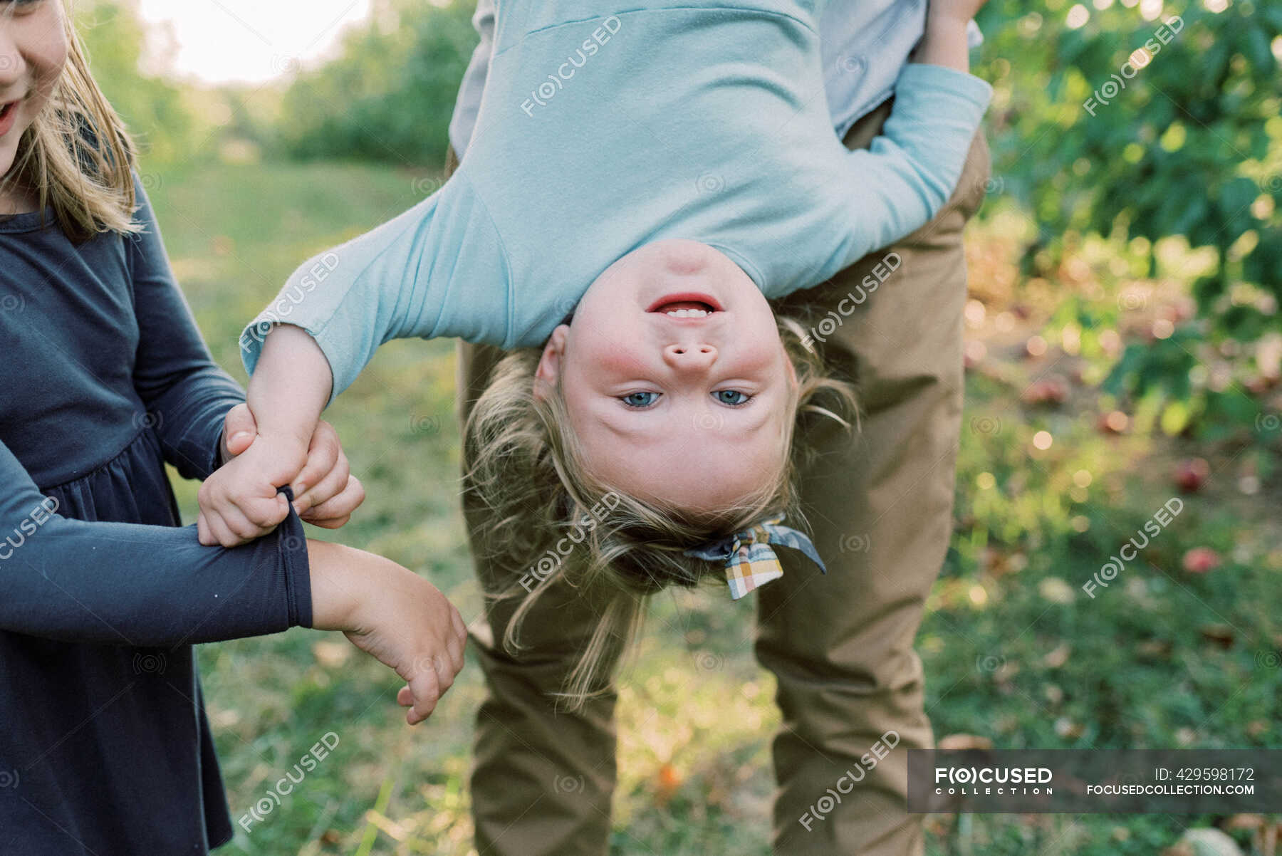 a-cute-toddler-girl-being-held-upside-down-with-her-sister-cheering